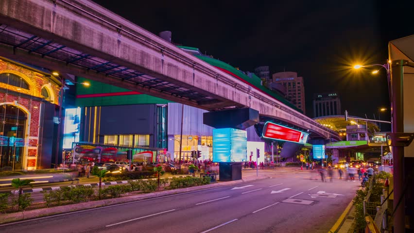 Timelapse of modern Asian city intersection at night. Car light trails, urban lights, ads, people cross streets, monorail train station, Kuala Lumpur Royalty-Free Stock Footage #1104471757