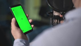 a man holds a phone with a green screen in his hands. he's in the recording studio. real time video. smartphone with green screen. close-up. High-quality FullHD video recording