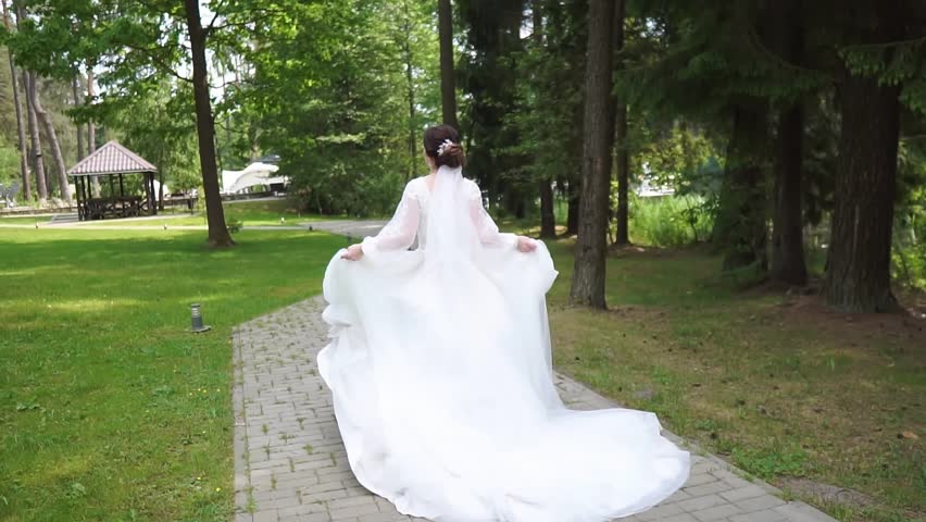 A beautiful bride in a luxurious white wedding dress runs along the path to meet the groom, rear view. Runaway Bride.  Royalty-Free Stock Footage #1104474479