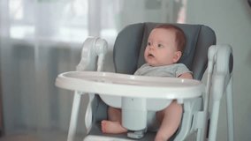 Cute baby boy of ten-months old sitting in a baby chair, mother gives wooden teether, infant holding toy shape of tooth, ECO toy made of natural materials concept. . High quality FullHD footage