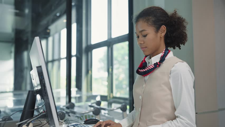 Young american african women airline ground staff worker in uniform working with computer in airport check in counter. Ground hostess airport reception at airline check in counter Royalty-Free Stock Footage #1104478387