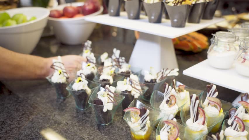 The waiter of the restaurant in the hotel makes a buffet table arrangement of delicacies fruits desserts for tourists' clients. Slow motion. | Shutterstock HD Video #1104480149