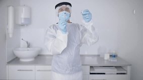 Crop focused professional male medical practitioner in surgeon gown gloves and face shield filling syringe with medication from vial while working in modern equipped hospital