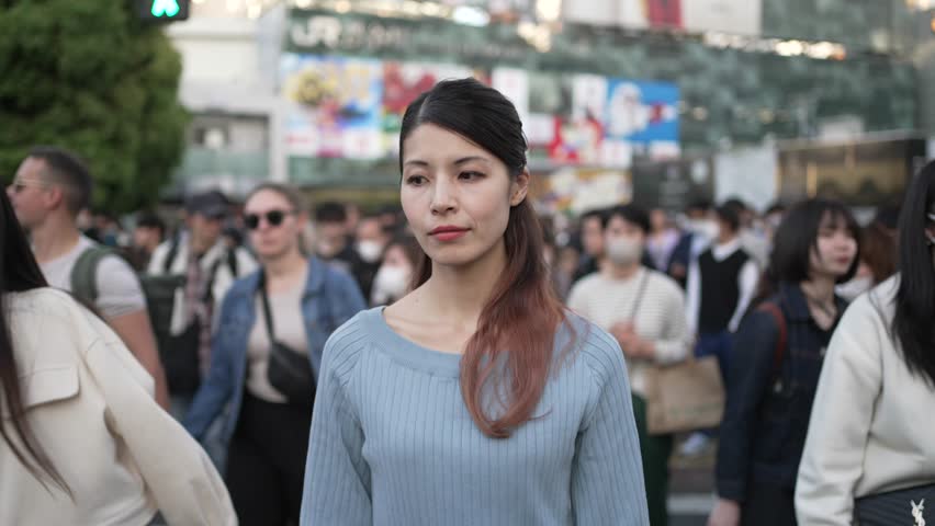 Japanese Woman crossing Shibuya Crossing in Tokyo Japan seen frontally wearing blue onepiece