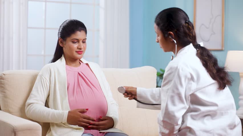 Shoulder shot of Indian doctor examining baby movement of pregnant woman belly by using stethoscope at home - concept of home health checkup, pregnancy care and medical treatment Royalty-Free Stock Footage #1104487155