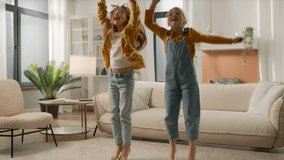 Two active funny little caucasian kids girls having fun moving play at home cheerful joyful children sisters friends playing together jumping dancing listening to music jump enjoy dance in living room - Powered by Shutterstock - Get 15% off with code: PIKWIZARD15