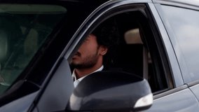 A young man with curly hair sticks his head out of the car window and sighs languidly. An Indian man in a business suit sits in a car and is indignant because of the traffic jam on the road.