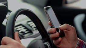 Cropped view of a man who sits behind the wheel of a car and slides on the screen of a smartphone. A man uses a smartphone while sitting in a car.