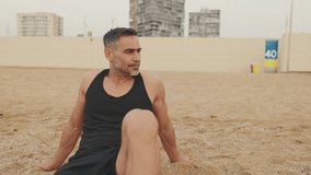 Middle aged athletic man relaxing after workout while sitting on the beach
