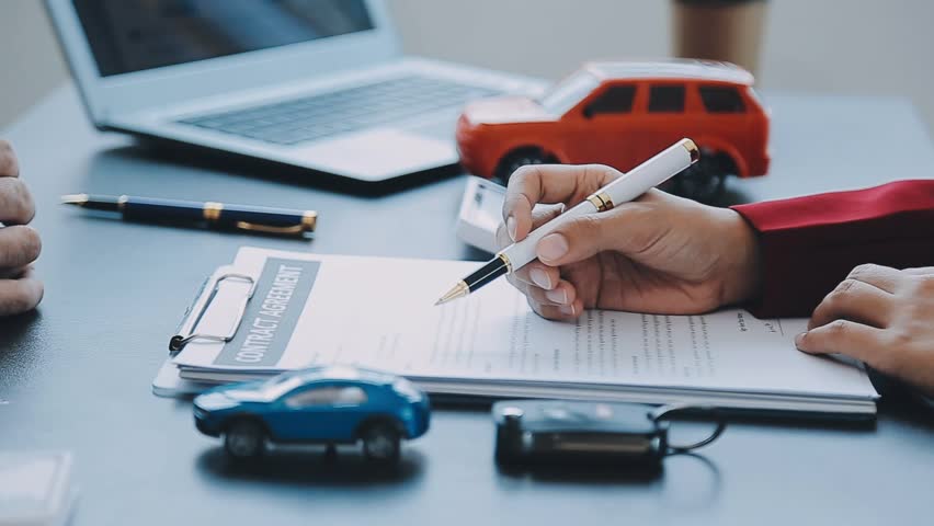 Closeup of Asian female signing car insurance document or lease paper contract or agreement. Buying or selling new or used vehicle with car keys on table.