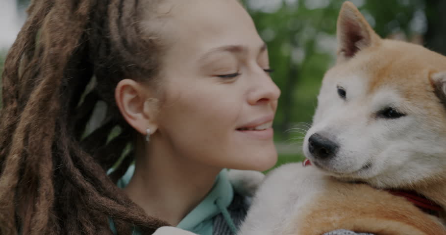 Close-up portrait of loving woman kissing cute shiba inu dog expressing love and happinness outdoors on summer day. Animal and affectionate human concept.