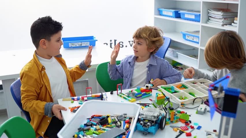 Robotics programming class. Children construct and code Robot. STEM education using constructor blocks and laptop tablet, remote control joystick. Technology educational development for school kids