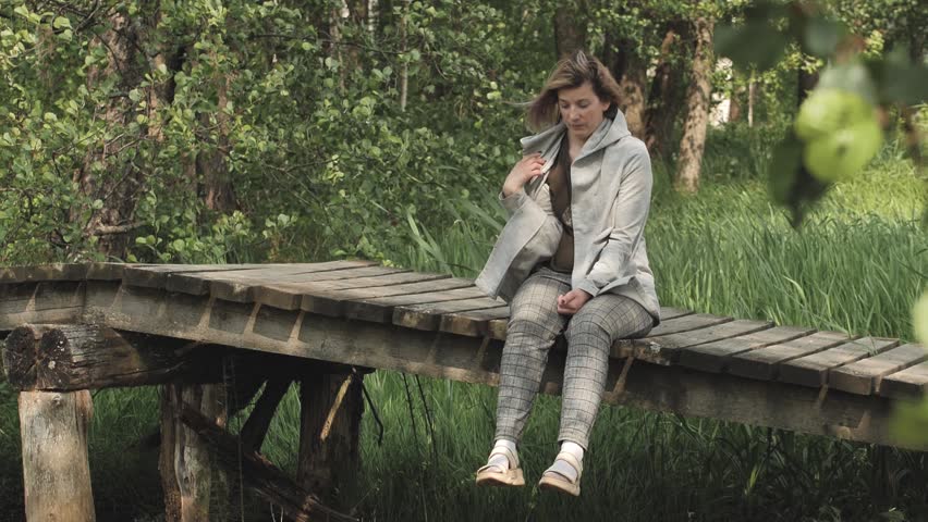 A woman is sitting on a wooden bridge in a depressed state. Close-up face of sad looking pensive woman suffering from loneliness depression. Unhappy vulnerable young woman dealing with stress | Shutterstock HD Video #1104498943