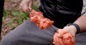 Close-up of a man's hands stringing pieces of marinated meat for frying on a grill with hot coals.