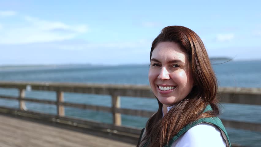 Smiling Caucasian woman looking at the camera excited. Background sea. Dressed in a green vest.