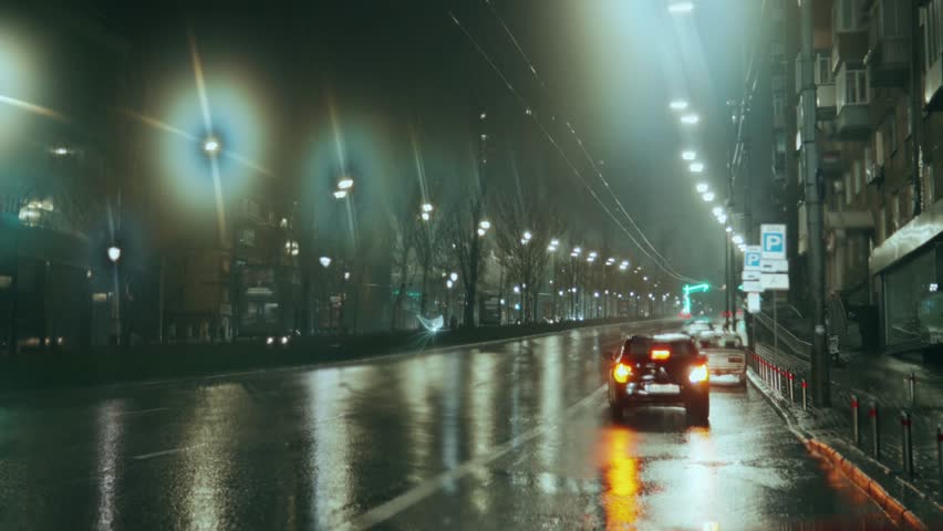 A parked car backs up against the background of wet asphalt with city lights