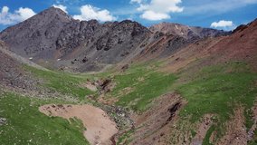 Aerial video of Mountain Spirits Lake in Altai mountains. Kurai mountain range. Mountains are rich in mercury deposits and red from cinnabar. Camera moves backwards.