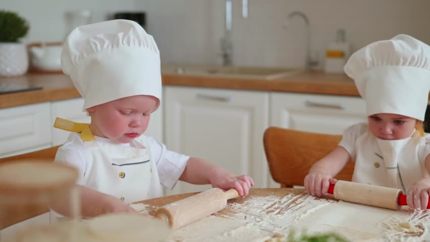 Adorable 3 years old boy and girl in chef hats and aprons rolling out pastry dough at the kitchen. Young helpers, preparing delicious pastry food. Royalty-Free Stock Footage #1104507587