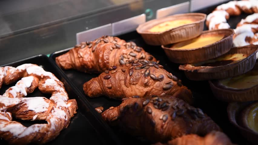 Close-up side view of bakery showcase with freshly cooked croissants and other pastries. Soft focus. Real time handheld video. No people. Puff pastry theme. | Shutterstock HD Video #1104508559
