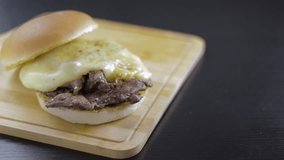 Barros Luco sandwich: beef with melted cheese. Hand placing bread cover, on black table and wooden board with copy space concept of typical Chilean food