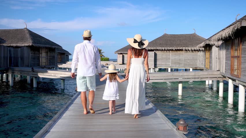 A elegant family walks over a wooden pier between water lodges in the Maldives islands during their tropical holidays