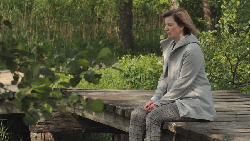 A woman is sitting on a wooden bridge in a depressed state. Close-up face of sad looking pensive woman suffering from loneliness depression. Unhappy vulnerable young woman dealing with stress | Shutterstock HD Video #1104515345