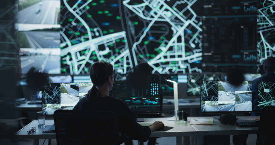 Establishing Shot: Dark Room with Multiethnic Specialists Working on Desktop Computers. Big LED Screen Shows Surveillance Satellite Data, City Map, and CCTV Traffic Footage Reports Royalty-Free Stock Footage #1104516835