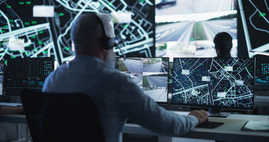 Senior Specialist in a Dark High-Tech Monitoring Room, Concentrated on a Call and Computer Work. Fleet Manager Using Headphones with Built-In Mic for Communication with Delivery Vehicles Royalty-Free Stock Footage #1104516931