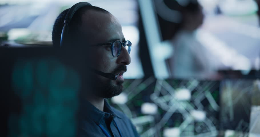 Portrait of a Surveillance Officer Wearing a Headset, Working in a Central Office Hub for Cybersecurity Operations, Control and Monitoring for Managing National Security and Technology Royalty-Free Stock Footage #1104516969