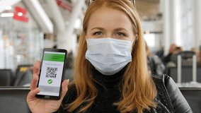 Portrait of a young woman in a medical mask and a leather jacket at the airport, she shows a QR code on her phone about vaccination against coronavirus. - Powered by Shutterstock - Get 15% off with code: PIKWIZARD15