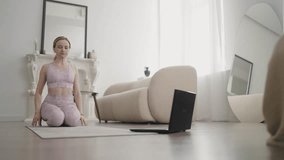 Young athletic girl doing yoga on video tutorial on laptop in bright room. Slow motion