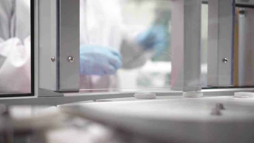 A doctor with a protective suit puts empty bottle of medicine to be filled with red pills in factory