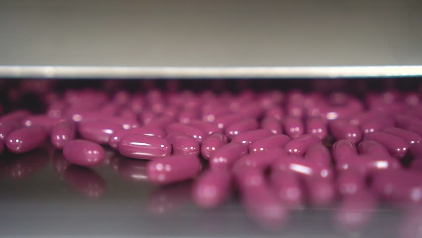 A closeup of fresh red pills out of the machine in the factory