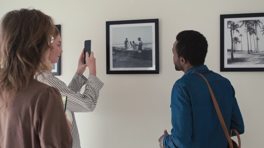 Group of visitors taking pictures of framed photo on wall while visiting exhibition in art gallery