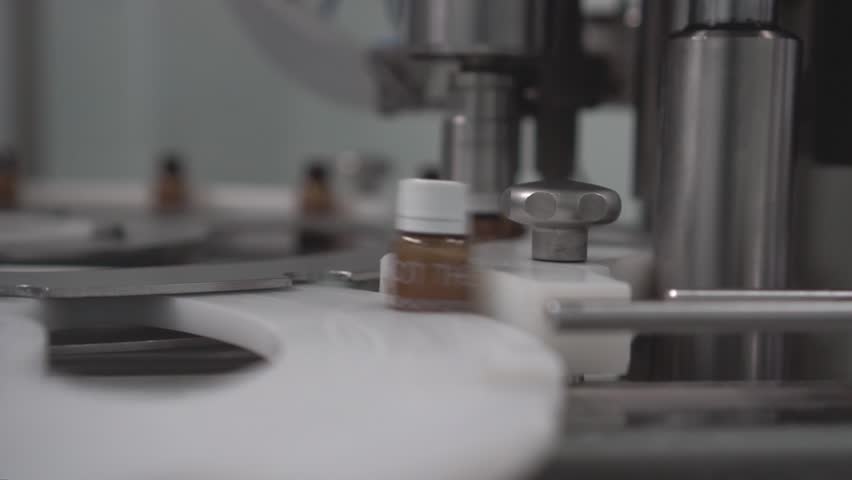 A closeup of an automation machine producing glass medicine bottles
