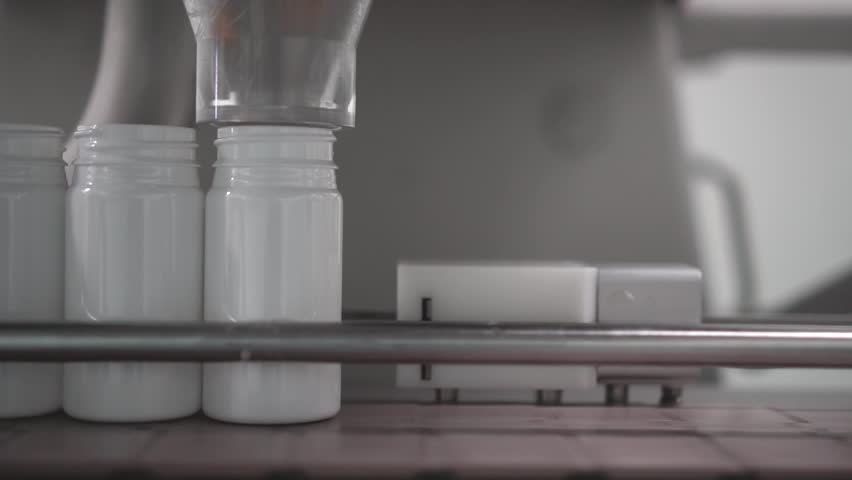 A closeup of automation machine filling white bottles medicine with red pills