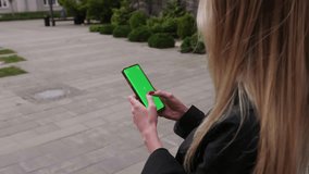 Woman holding smartphone with chroma key outside urban city. Young female person using phone with green screen outdoor.