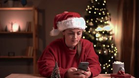 Joyful Caucasian woman in santa hat sitting in cozy room near xmas tree using smartphone with surprised face win christmas lottery. Happy New Year. Merry Christmas - Powered by Shutterstock - Get 15% off with code: PIKWIZARD15