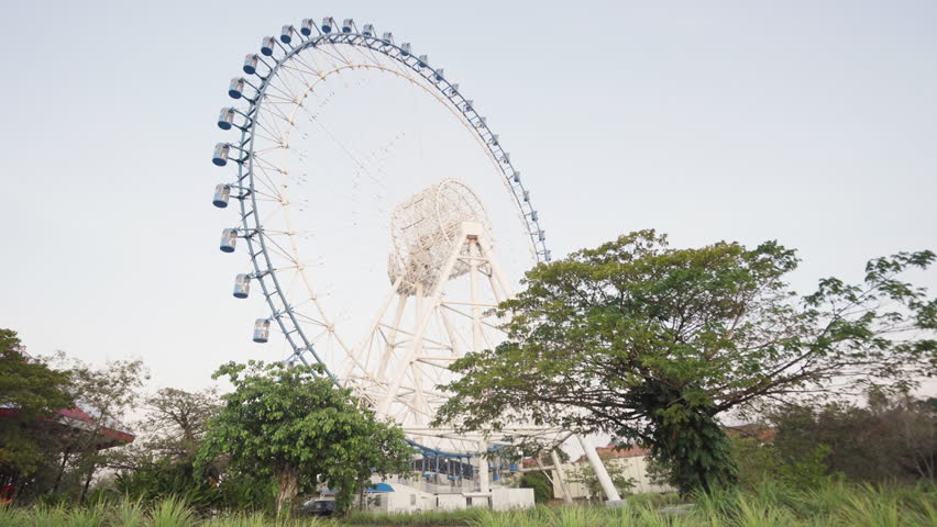 A low-angle shot from a grassy ground showing a ferris wheel near the trees in a park in Cambodia
