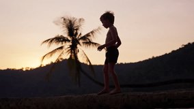 A video of a boy walking carefully on a tree trunk at a beach in Thailand during sunset