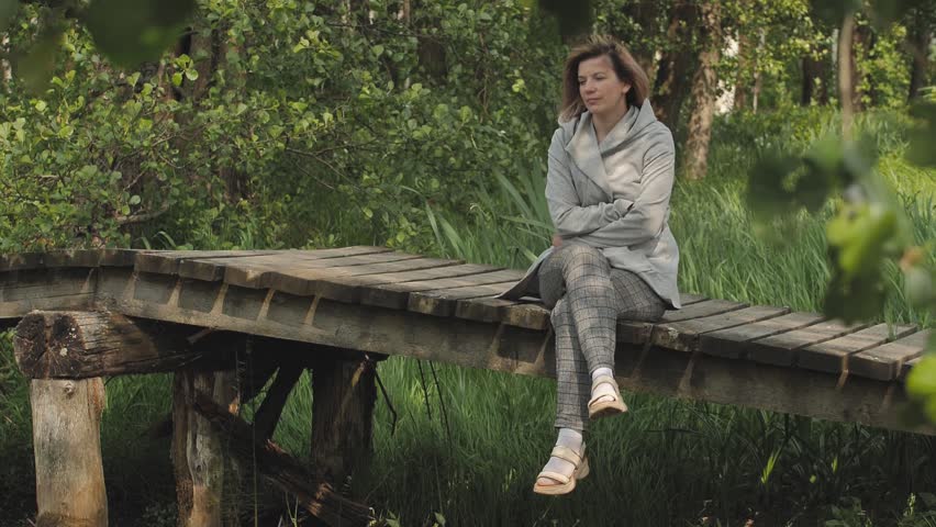A woman is sitting on a wooden bridge in a depressed state. Close-up face of sad looking pensive woman suffering from loneliness depression. Unhappy vulnerable young woman dealing with stress | Shutterstock HD Video #1104549127