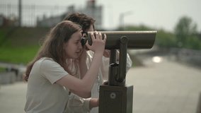 teenagers, a girl and a boy look through a spyglass in the park. real time video. teenagers in the park in summer. High quality Full HD video recording