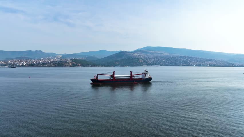 Full aerial view of red cargo ship carrying weather vane propeller, advancing off the Aegean Sea, Izmir Bay