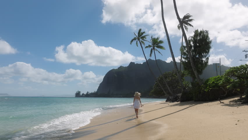 Slow motion woman walking by tropical sandy beach leaving footprints. Female tourist on summer vacation on paradise island of Oahu. Woman in white mini boho dress on green Hawaiian islands, USA 4K Royalty-Free Stock Footage #1104554811