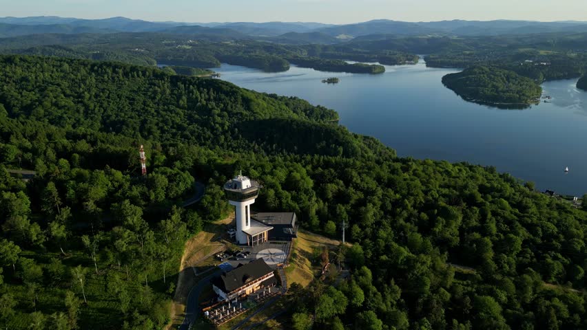 Panoramic view from the drone during sunset, on the Solińskie lake overlooking the modern gondola cable car with the lookout tower over the Solina water dam, in the Polish Bieszczady Mountains, Poland