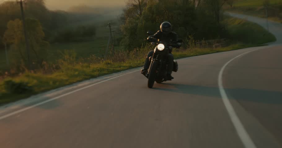 Slow-motion shot of a man driving a road curve on a motorcycle during sunset. Royalty-Free Stock Footage #1104561763