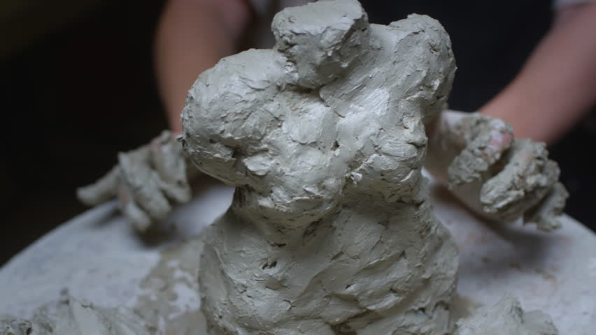 A talented sculptor girl creates a sculpture of a fat woman from clay with her hands. Body positive in art. The female strikes with her fingers wet clay on an unfinished figure. Perfect body shapes