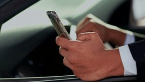 A man sits in a car and taps on the smartphone screen. Cropped view of a man who uses a smartphone while standing in a traffic jam.