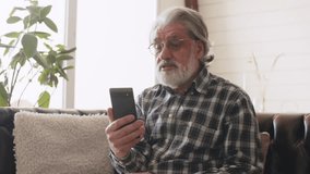 Senior man with beard having video call. Grandfather in glasses and checkered shirt talking on the phone