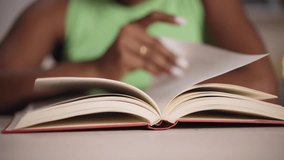 Video close up hands of young black woman at home reading a book. African American girl sitting at a desk. People passionate about literature. Selective focus on paperback.